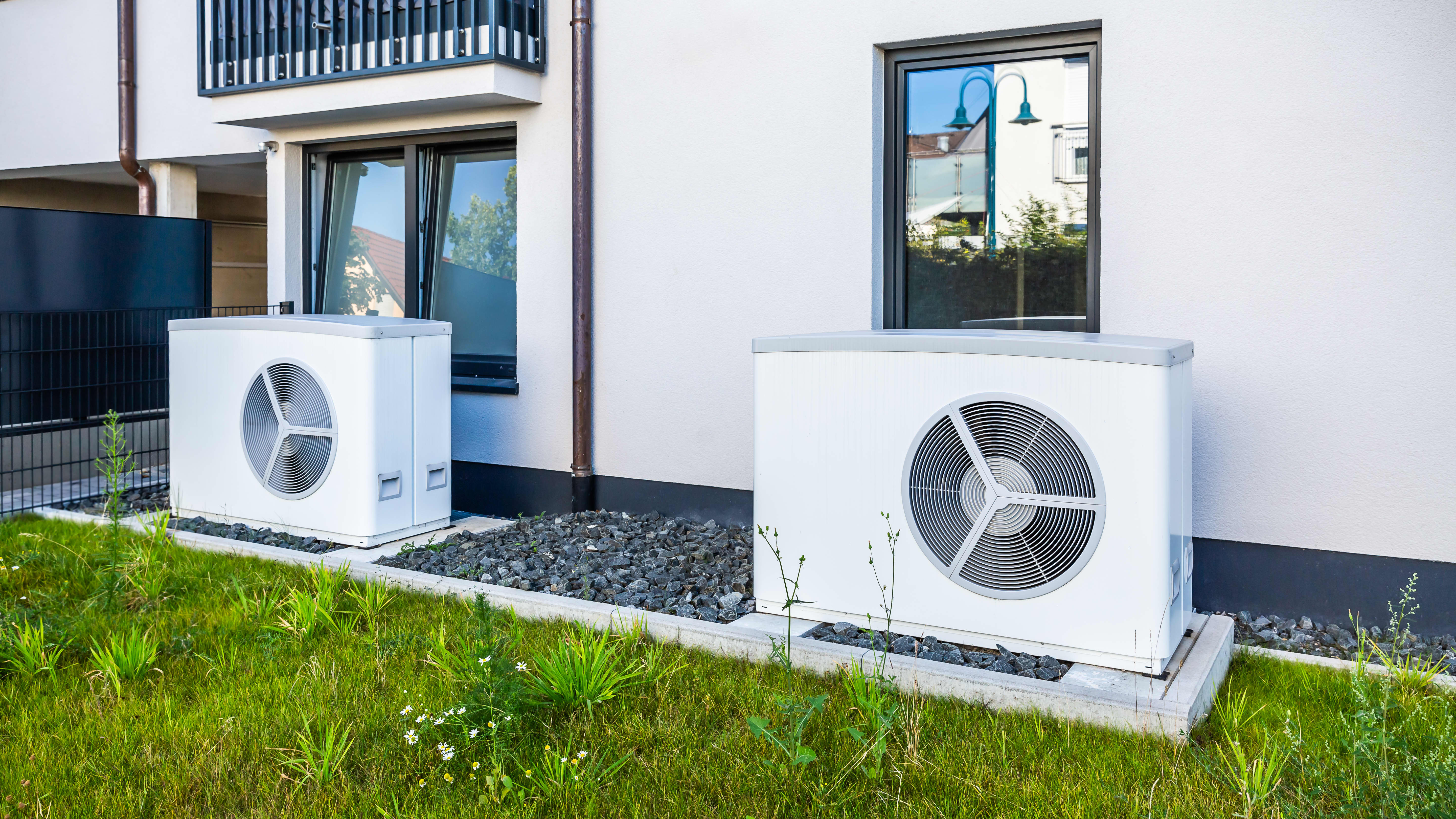 Zwei weiße Wärmepumpen vor weißer Fassade eines Wohngebäudes, davor grünes Gras