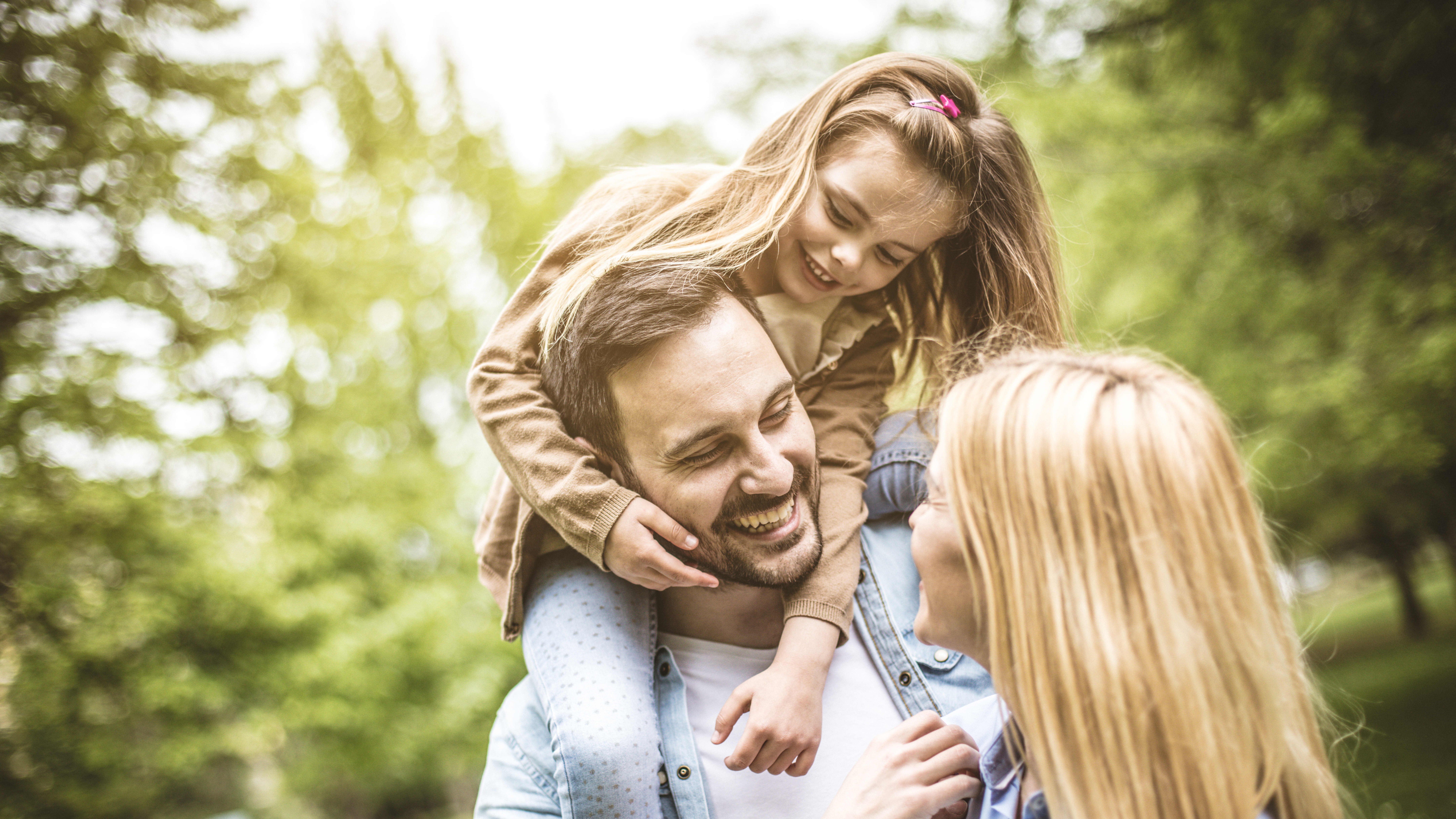 Junges lachendes Paar im Grünen, der Vater hat seine Tochter auf den Schultern