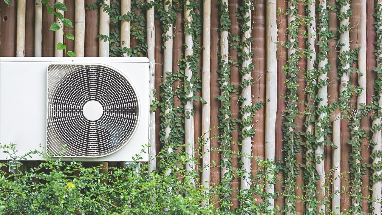 Luftwärmepumpe vor einer bepflanzten Wand
