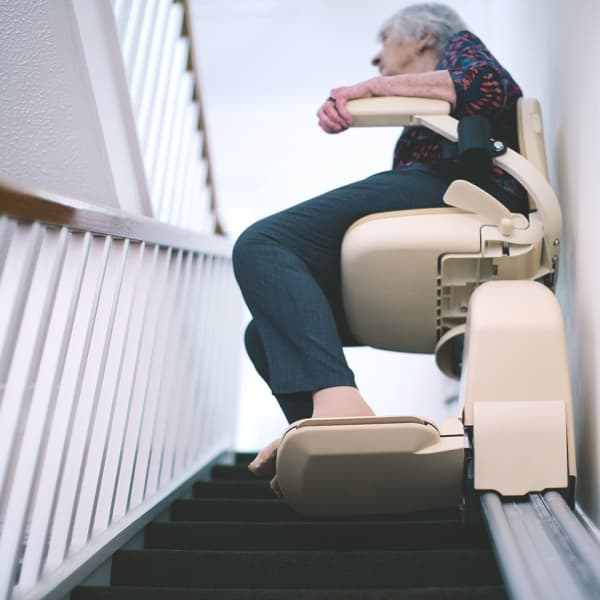 Blick von unten auf eine ältere Dame in einem Treppenlift für schmale Treppen