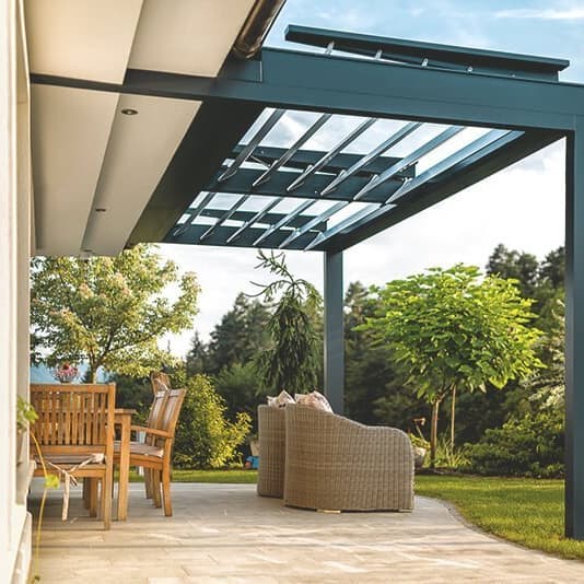 Angebaute Terrassenüberdachung mit verschiedenen Sitzgelegenheiten darunter vor einem gepflegten Garten.