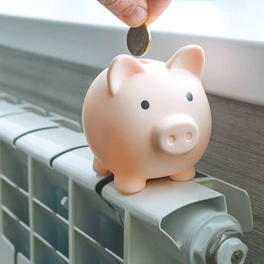 Sparschwein auf einem Heizkörper wird mit einem Euro gefüllt.