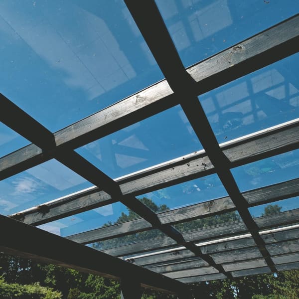 Terrassenüberdachung mit Glasdach und Holzrahmen bei blauem Himmel.