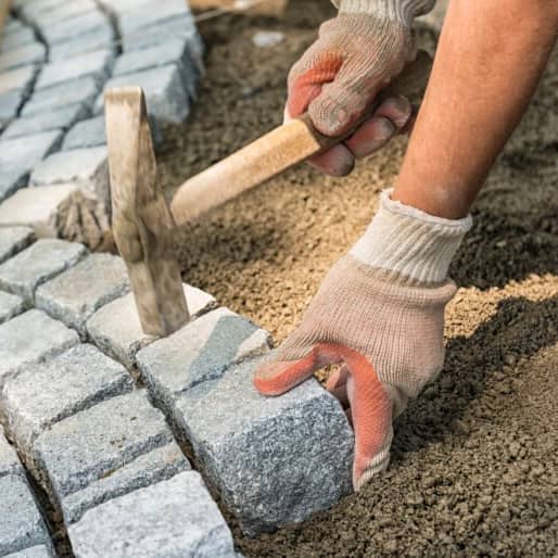 Auf der Terrasse werden Pflastersteine von einem Handwerker verlegt.