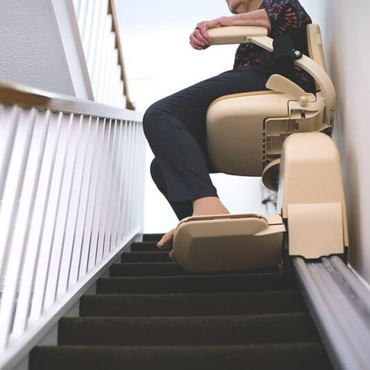 Person sitzt im Sitzlift und fährt die Treppe hoch.