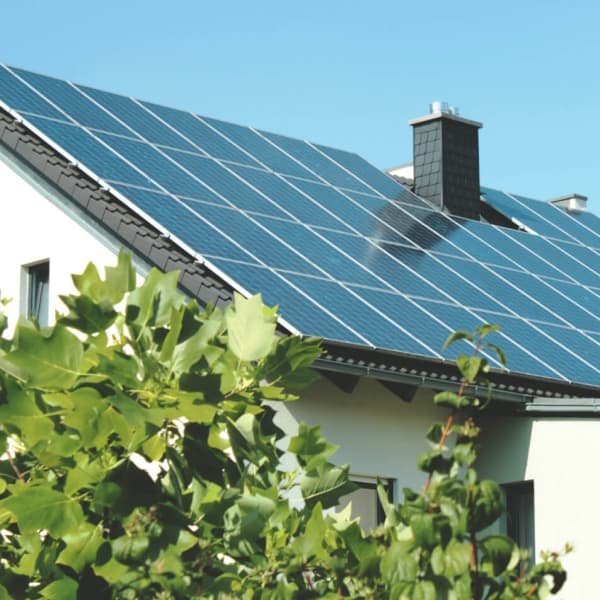 Sonnenbeschienenes Hausdach mit moderner Photovoltaikanlage in einer idyllischen Wohngegend. Nachhaltige Energiegewinnung inmitten von grüner Natur.