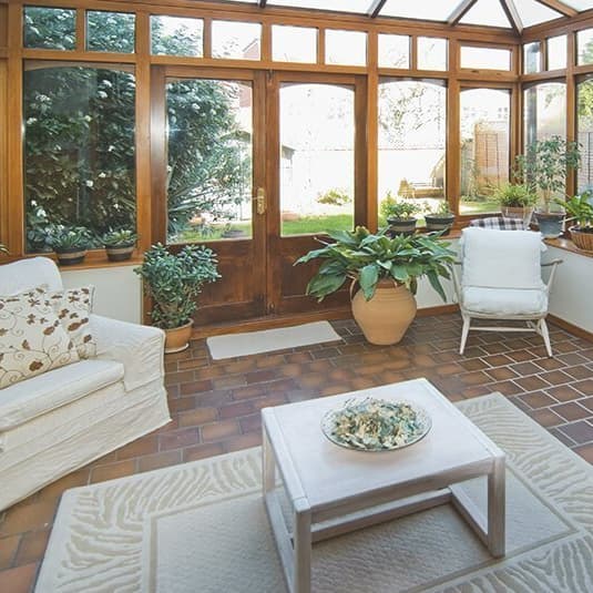 Wintergarten mit Holzrahmen, Terrakottafliesen und Pflanzen