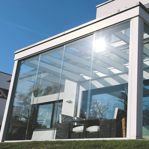 Moderner Wintergarten mit Glaswänden, Flachdach und weißen Aluprofilen.
