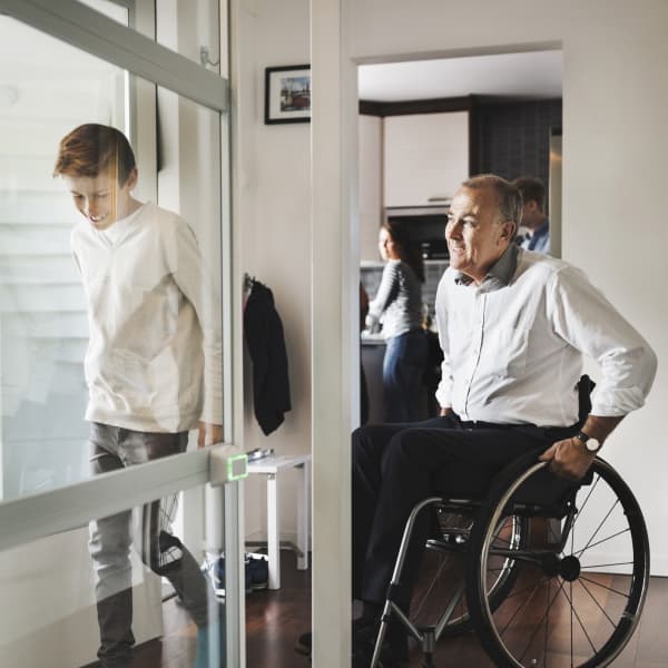 Ein älterer Mann im Rollstuhl zu Hause mit seinen Kindern und Enkel vor Rollstuhllift.