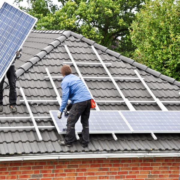 Handwerker montieren zwei Solarpanels auf ein Hausdach