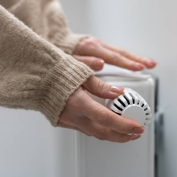 Eine Hand dreht die Heizung auf, die andere liegt auf dem Heizkörper und prüft, ob es warm wird