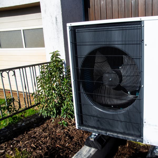 Weiße Luft-Wasser-Wärmepumpe vor Einfamilienhaus