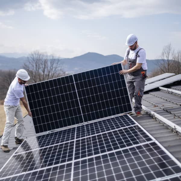 Zwei Installateure montieren ein Solarmodul auf ein Hausdach.