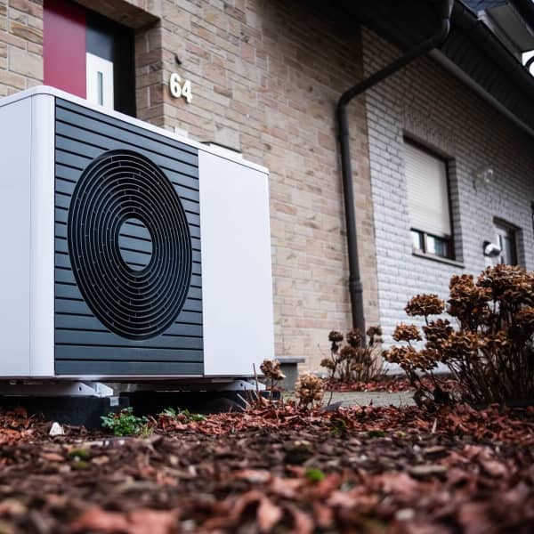 Luftwärmepumpe im Herbst vor einem Wohnhaus mit hellbrauner Steinfassade