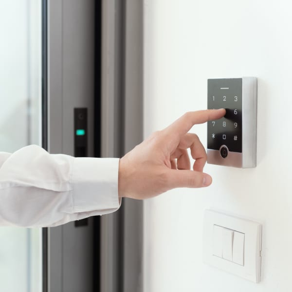 Hand eines Mannes tippt eine Zahl auf dem Nummernpad einer Alarmanlage an