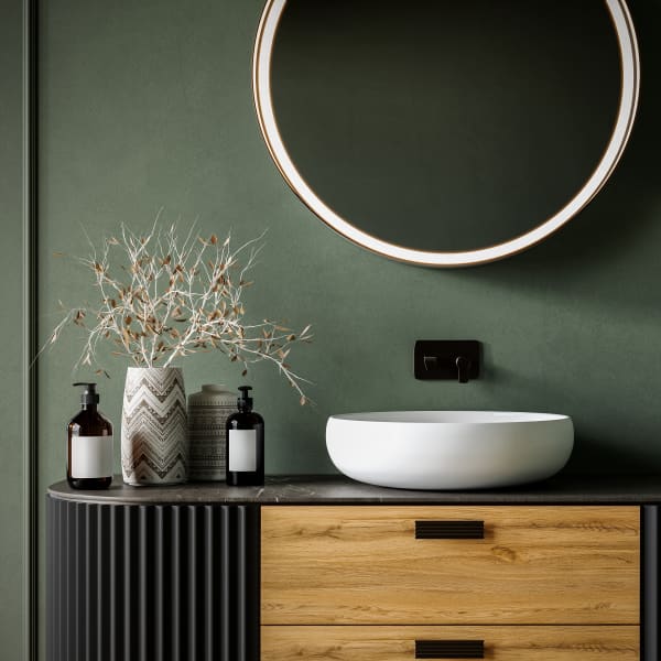 Freistehender Waschtisch mit rundem Spiegel vor grüner, geputzter Wand