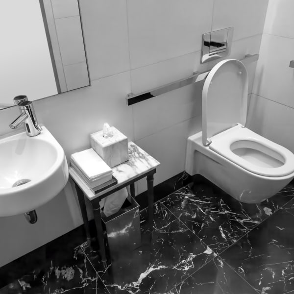 Modernes, hell gefliestes Badezimmer mit dunklen Bodenfliesen und Haltegriffen neben Toilette und Waschtisch