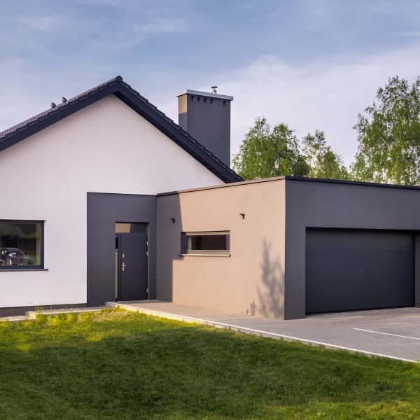 Garage aus Beton mit Seitenfenster und Sektionaltor vor einem Einfamilienhaus.