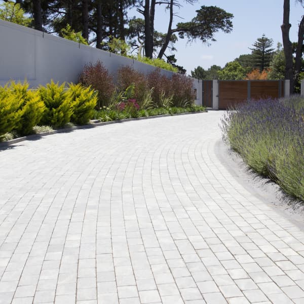 Lange, gepflasterte Auffahrt mit Blumenbeeten daneben.