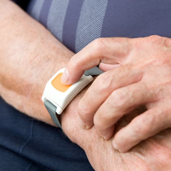 Mann in blauem T-Shirt drückt gelben Notrufknopf an einem Armband.