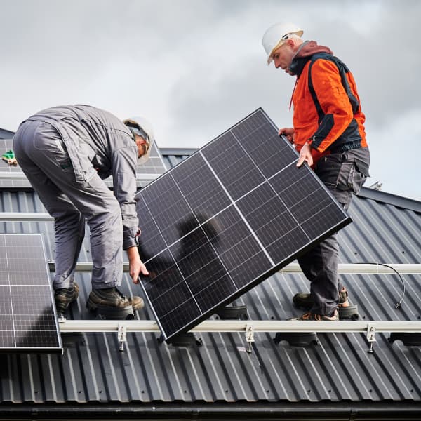 Solarmodule werden auf einem Hausdach von zwei Handwerkern montiert.