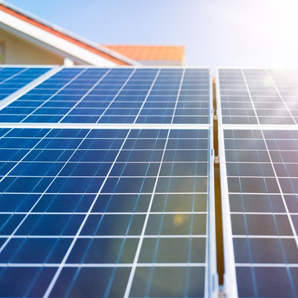 Nahaufnahme von blauen Solarmodulen mit einem klaren Rastermuster, beleuchtet von hellem Sonnenlicht. Die Module gehören zu einer Solaranlage auf einem Wohnhaus und erzeugen erneuerbare Energie zur nachhaltigen Stromversorgung.