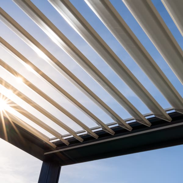 Sonne scheint durch offene Lamellen einer Terrassenüberdachung.