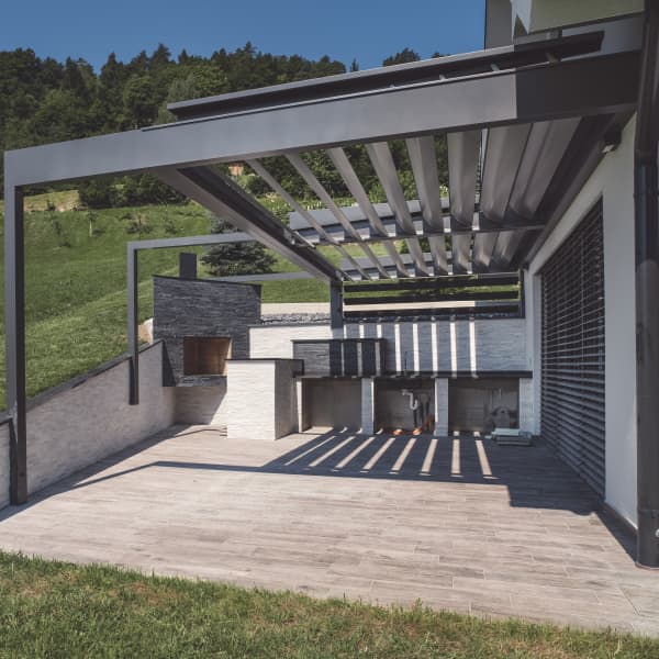 Terrassenüberdachung aus Aluminium mit Lamellendach, am grünen Hang gebaut.