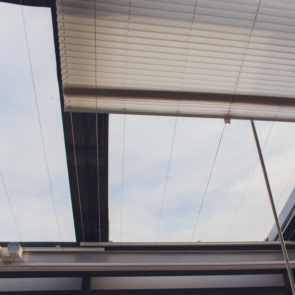 Ein Plissee unter dem Glasdach einer Terrassenüberdachung.