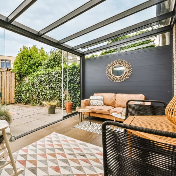 Terrassenüberdachung aus Aluminium mit aufschiebbaren Glaswänden und einer festen Seitenwand.