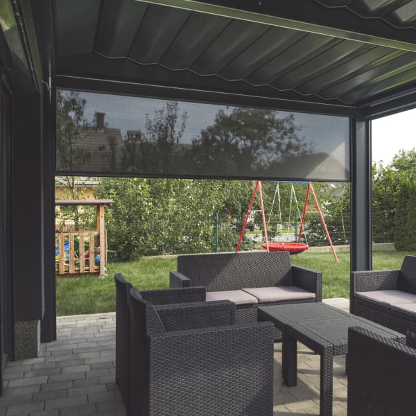 Terrassenüberdachung mit Sitzgruppe und einem halb heruntergefahrenen Seitenrollo