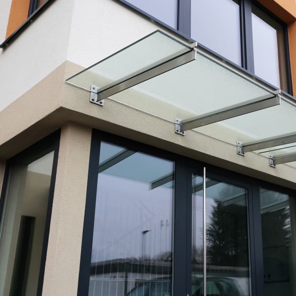 Ein Vordach aus Glas über einem Eingangsbereich eines Mehrfamilienhauses