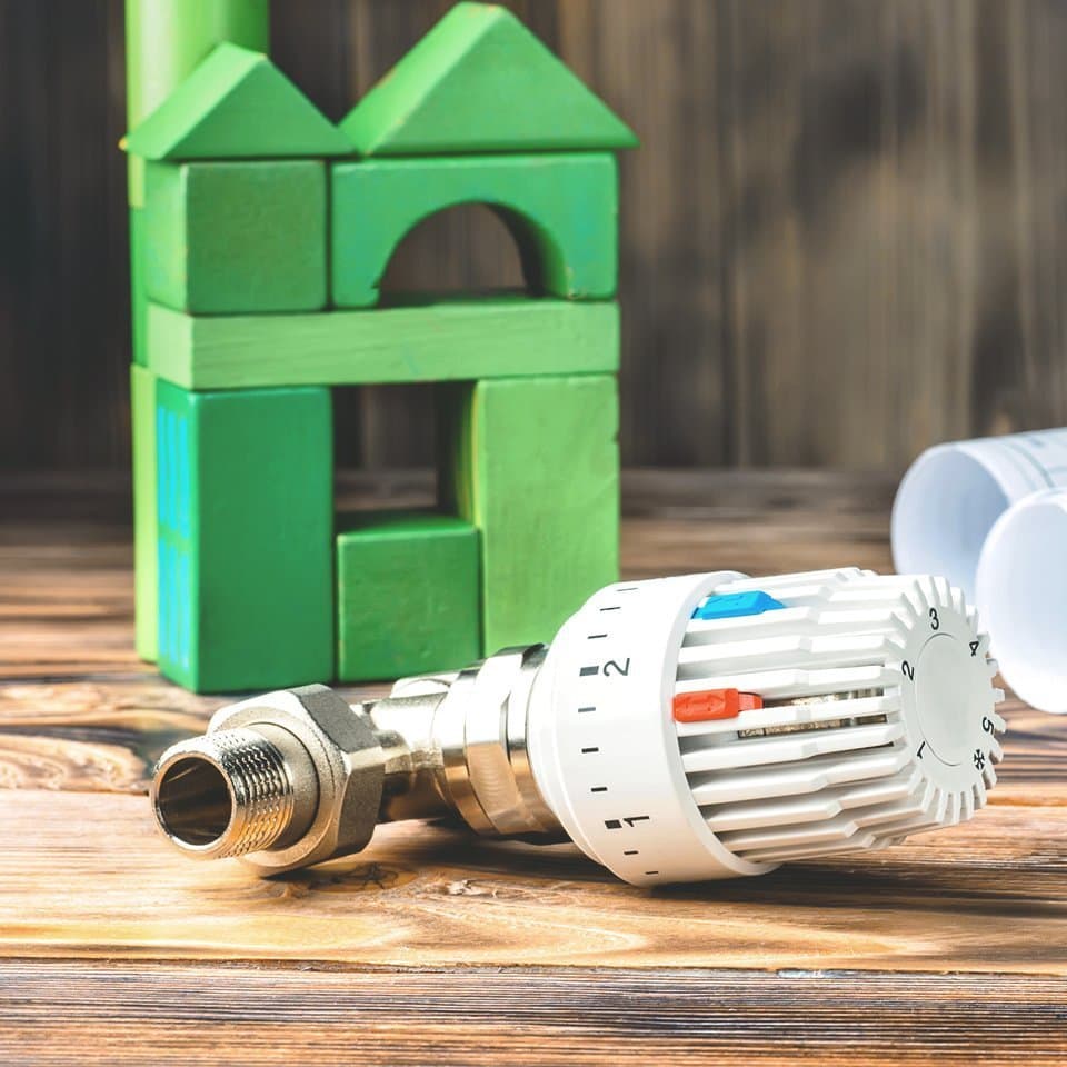 Thermostat neben Bauzeichnungen und grünem Haus
