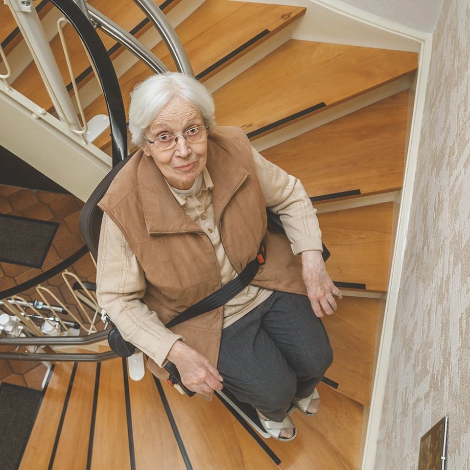 Frau im Stehlift fährt die Treppe hoch