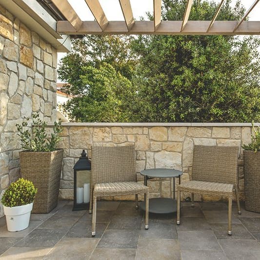 Pergola aus Holz mit festen Lamellen über einer Terrasse mit zwei Stühlen.