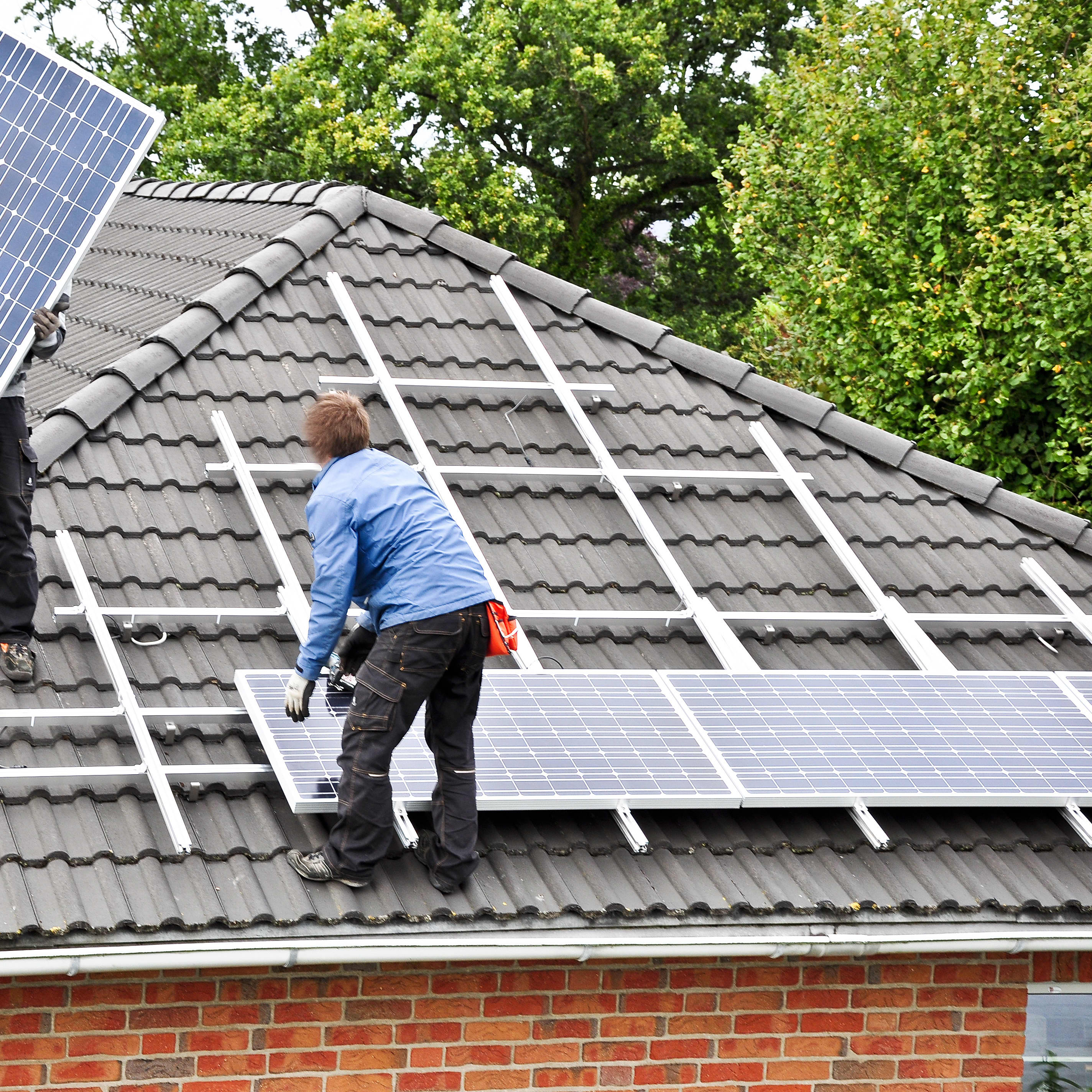 Handwerker montieren zwei Solarpanels auf ein Hausdach