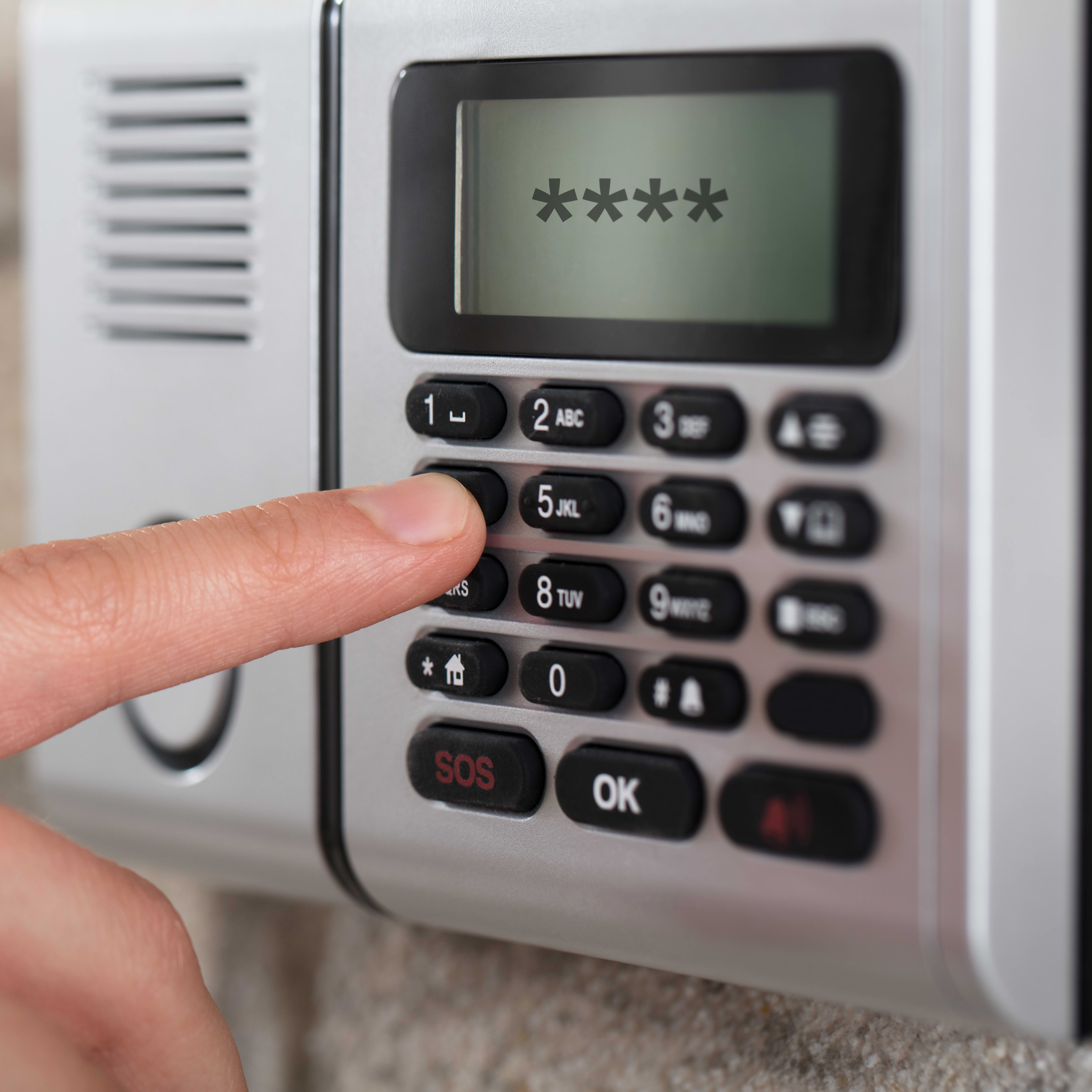 Nahaufnahme der Hand einer Person, die den Sicherheitscode an einer Alarmanlage eingibt