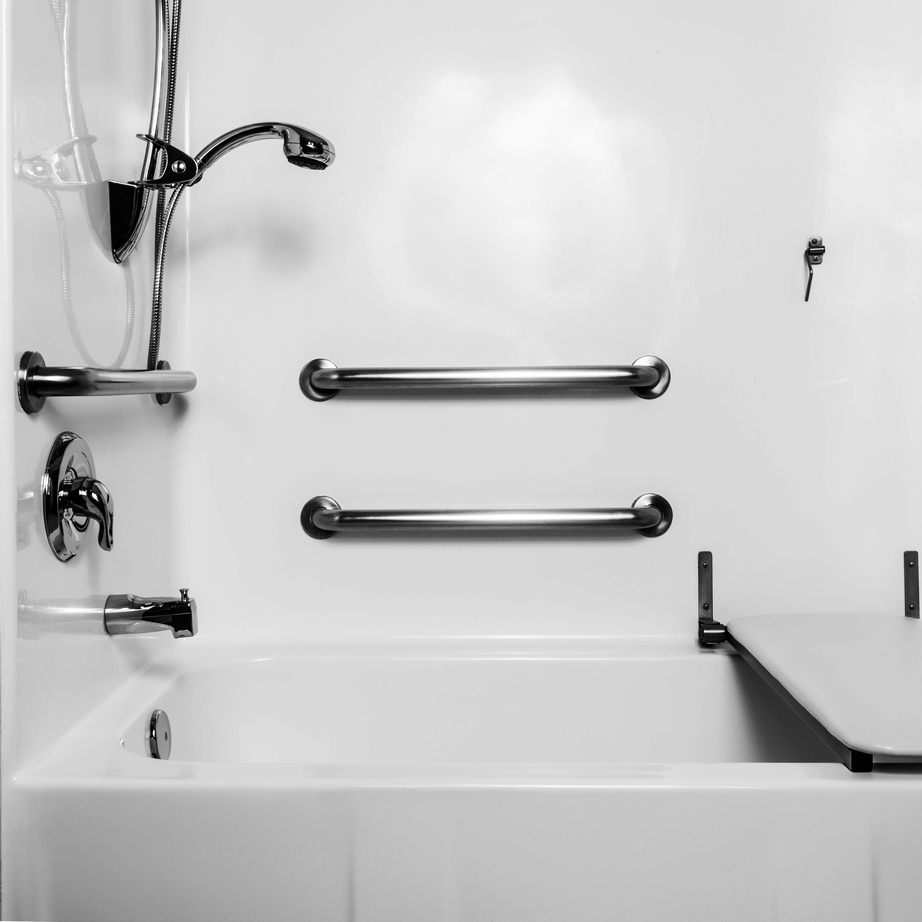 Badewanne mit Haltegriffen, Klappsitz und verstellbarem Duschgriff in einem weiß gefliesten, alters- und behindertengerechten Badezimmer
