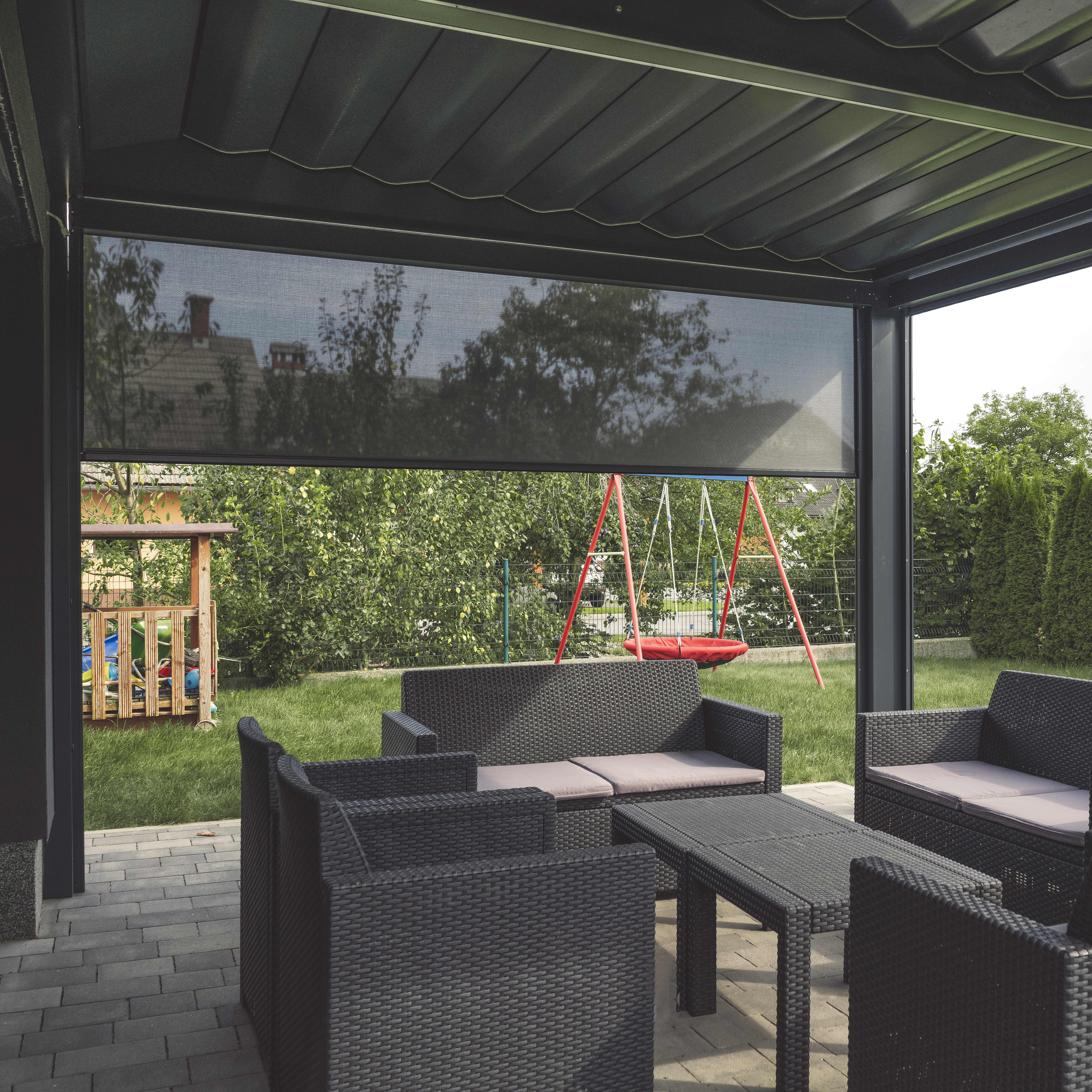 Terrassenüberdachung mit Sitzgruppe und einem halb heruntergefahrenen Seitenrollo