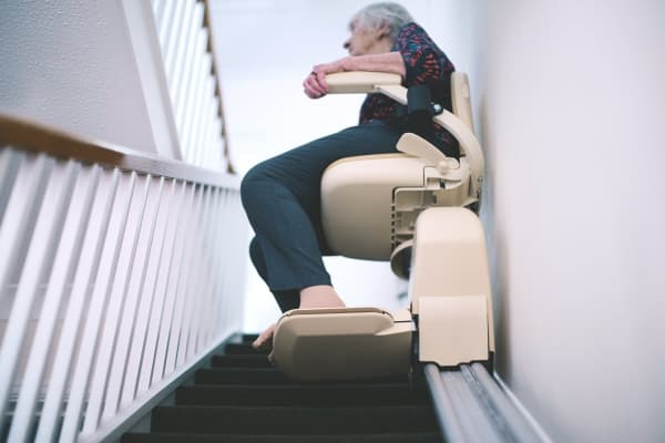 Blick von unten auf eine ältere Dame in einem Treppenlift für schmale Treppen