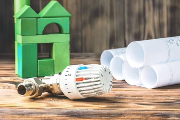 Thermostat neben Bauzeichnungen und grünem Haus