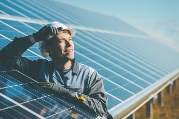 Bauarbeiter steht zwischen blauen Solarpaneels und guckt in den blauen Himmel
