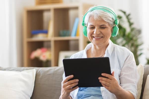 Frau schaut auf Tablet mit Kopfhörern auf dem Kopf