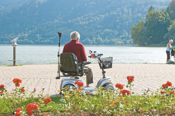 Älterer Mann sitzt auf Elektromobil und genießt den Ausblick aufs Wasser