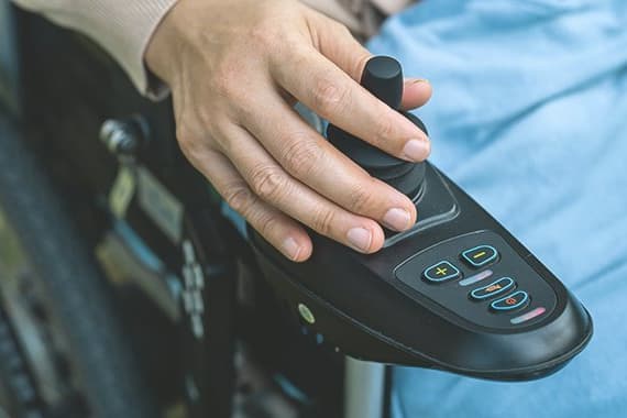 Hand lenkt Elektrorollstuhl mit Joystick
