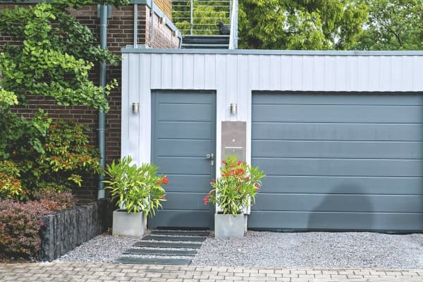 Stahlgarage mit Flachdach und Seitentür neben Wohnhaus