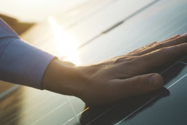 Eine Hand auf einem Solarpanel, im Hintergrund spiegelt sich die Sonne auf weiteren Solarzellen