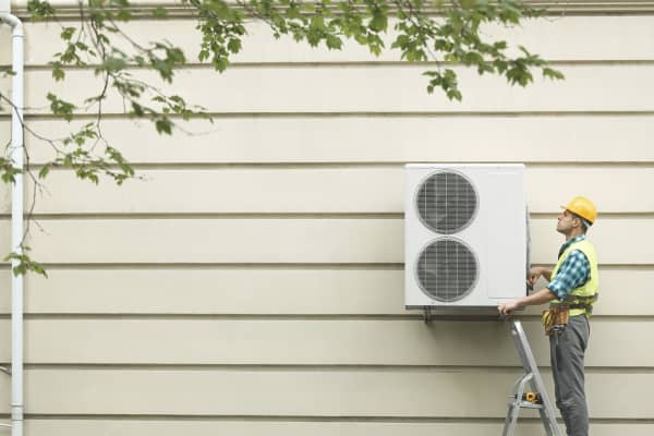 Bauarbeiter montiert Wärmepumpe an eine Häuserwand