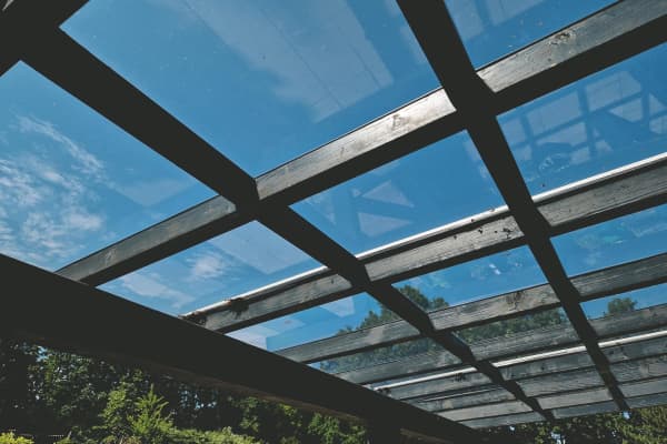 Terrassenüberdachung mit Glasdach und Holzrahmen bei blauem Himmel.