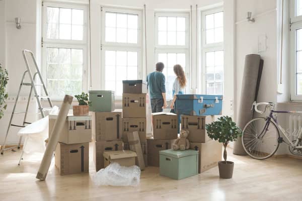 Ein Paar, Umzugskisten, Pflanzen, eine Leiter und ein Fahrrad stehen in der Mitte eines hellen Raums